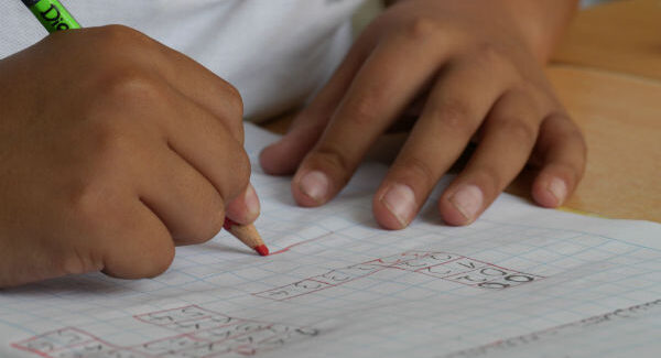 Bild på två händer. I den ena handen håller personen en penna.